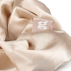 Nahaufnahme vom beige Seiden Scrunchie mit dem Logo.