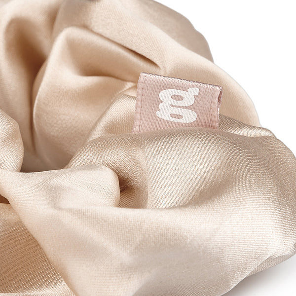 Nahaufnahme vom beige Seiden Scrunchie mit dem Logo.