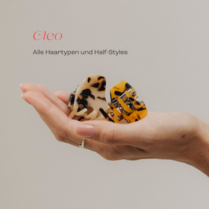 Hand mit zwei Haarclips in Schildpatt-Optik – links in hellbraun-schwarz gemustert, rechts in honiggelb-schwarz gemustert. Darüber der Schriftzug ‚Cleo – Alle Haartypen und Half-Styles‘.