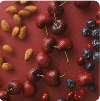 Roter Hintergrund und darauf liege Kirschen, Mandeln, Blaubeeren und Joahnnisbeeren. Es sind einige Wassertropfen auf den Produkten.