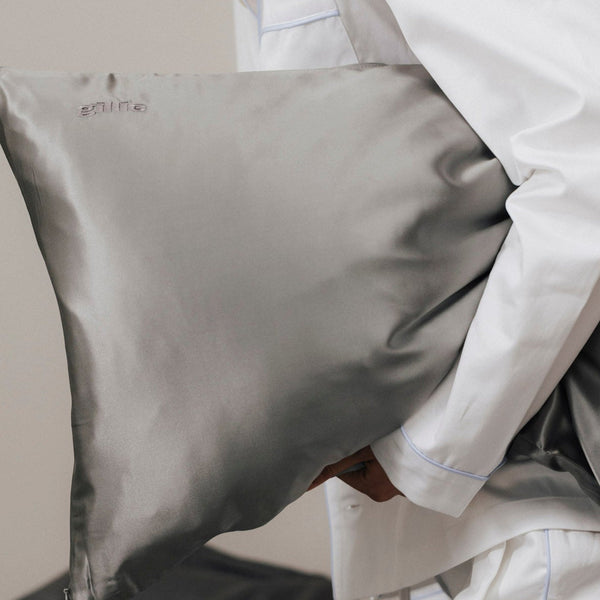 Frau in weißem Pyjama hält ein graues Seidenkissen mit gillie-Logo im Arm.