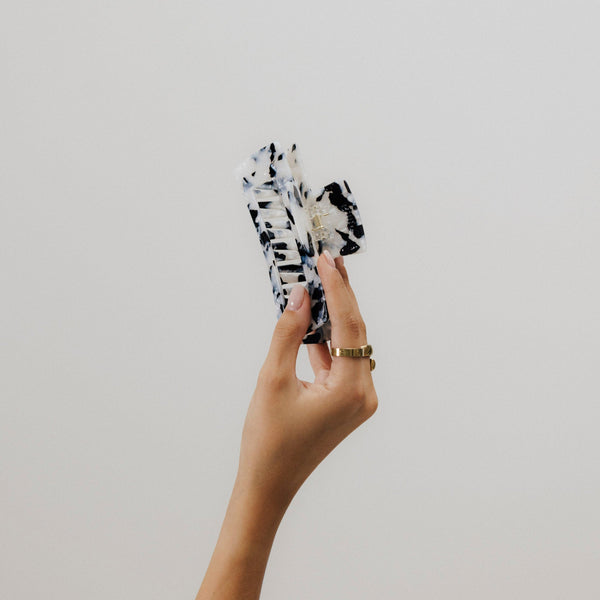Hand hält unsere Tortoise-Haarklammer in schwarz-weiß aus Bio-Acetat in die Luft – Fokus auf Form, Muster und Qualität.
