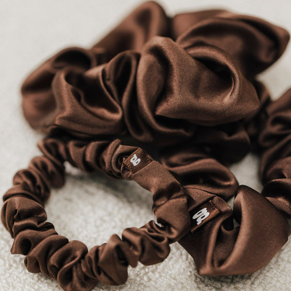 Nahaufnahme mehrerer brauner Scrunchies aus glänzender Maulbeerseide auf hellem Untergrund.