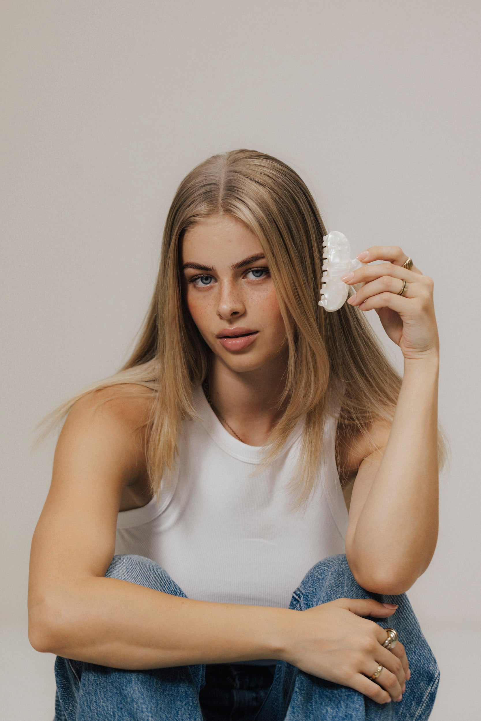 Blonde Frau hält eine shellfarbene Haarklammer (8,5 cm) und sitzt auf dem Boden.