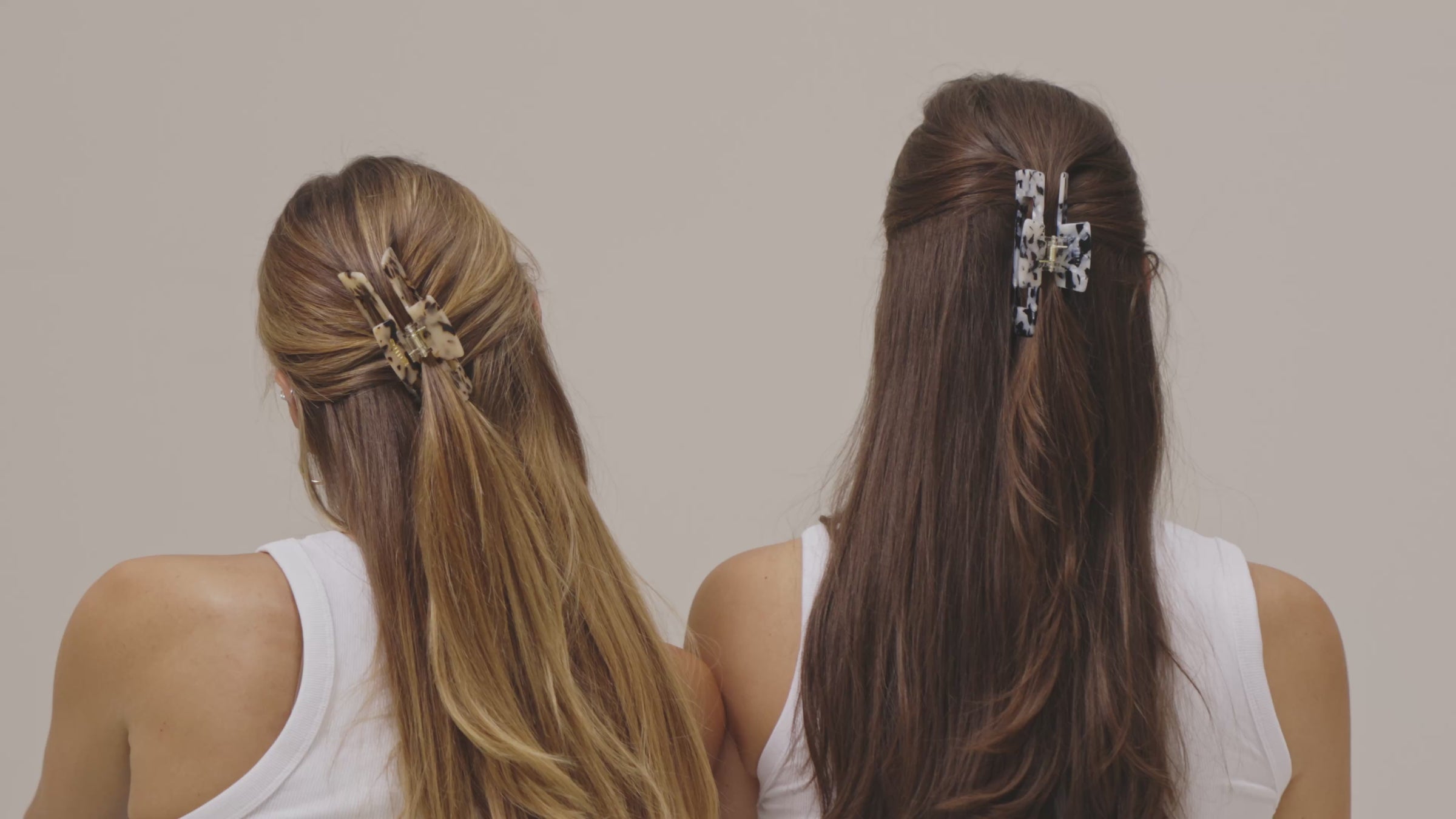 Junge Frau steht entspannt im Sommerlook vor einer weißen Wand und steckt sich langsam und elegant eine große, goldene Gillie-Haarklammer ins Haar. Ihr Stil wirkt modern und lässig zugleich.