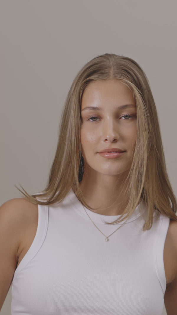 Frau mit dunkelblonden Haaren bindet sich einen Zopf mit einem braunen Scrunchie aus Maulbeerseide.