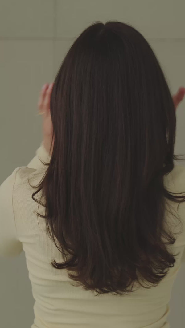 Frau mit dunklen Haaren wird von hinten gefilmt, während sie sich die Haare mit einer shellfarbenen Haarklammer hochsteckt.