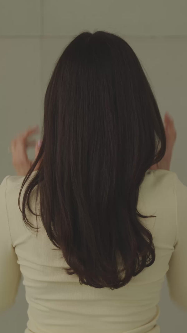 Frau mit dunklen Haaren wird von hinten gefilmt, während sie sich die Haare mit einer schwarzen, weißen Haarklammer hochsteckt.